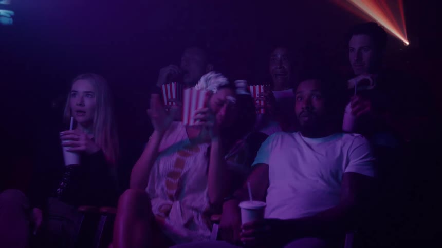 A group of people react in fear while watching a scary movie in a dark theater