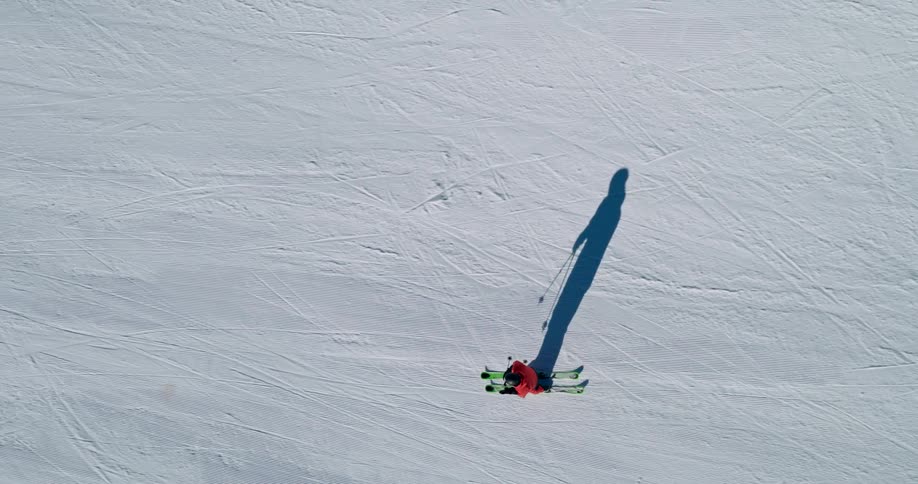 Top shot of a lone skier skiing down a vast tracked snow slope casting a long shadow