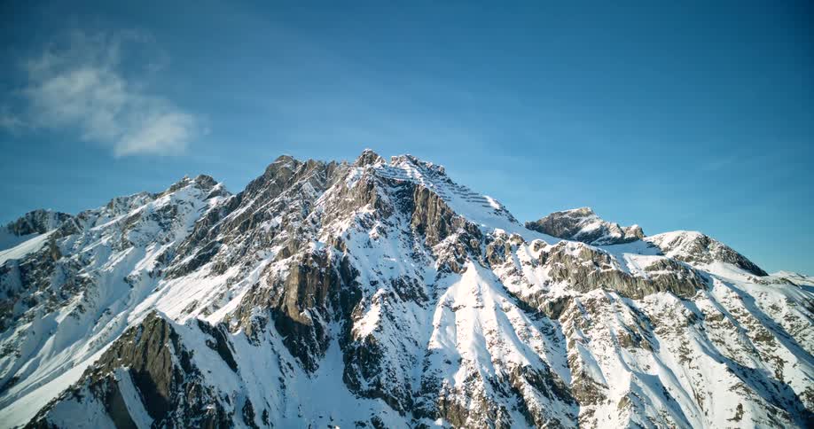 Aerial view of snow falling on a rugged mountain on a sunny winter day