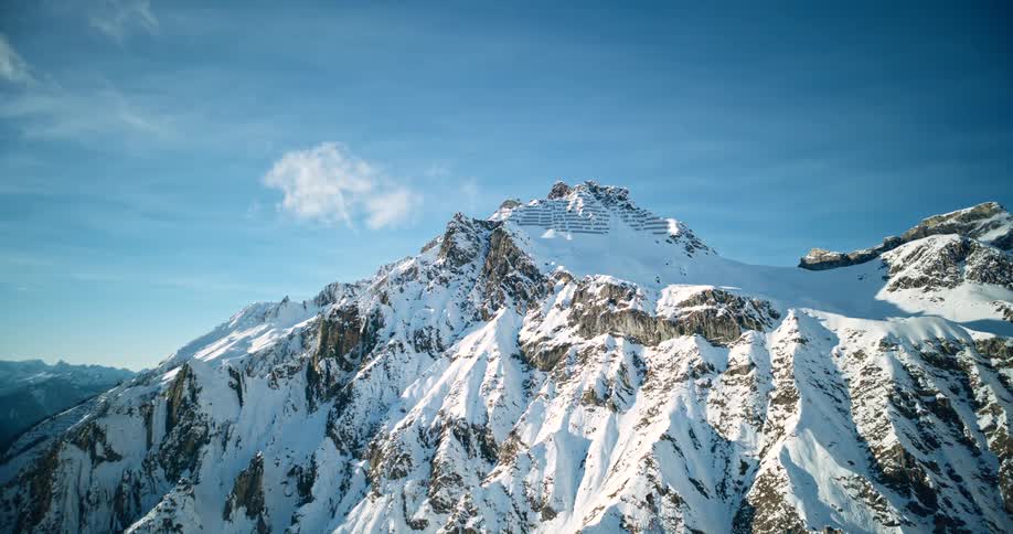 An aerial shot captures a majestic snowcovered mountain peak with steep rocky faces