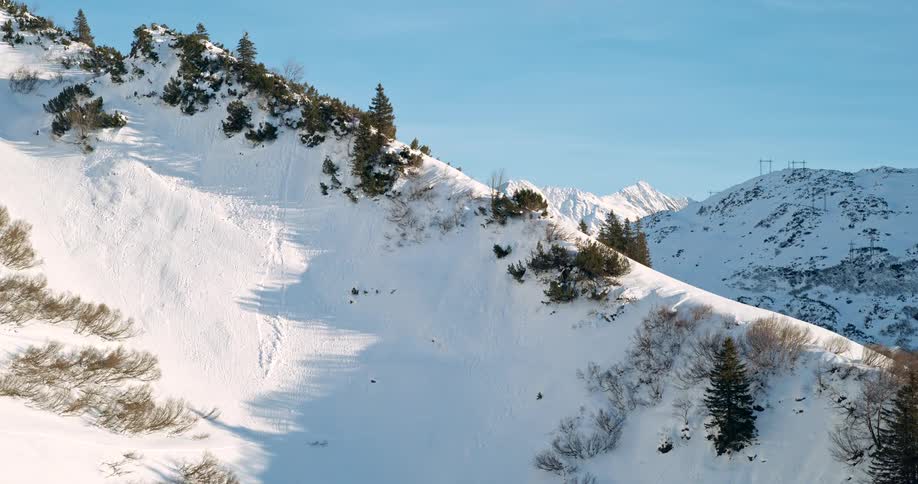 impressive panning shot of a large steep mountainside covered in deep snow