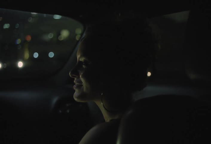 Woman sitting in a moving car at night with a happy expression