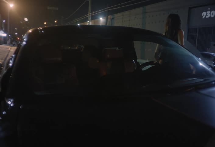 Two women get out of a dark van parked on an urban street at night