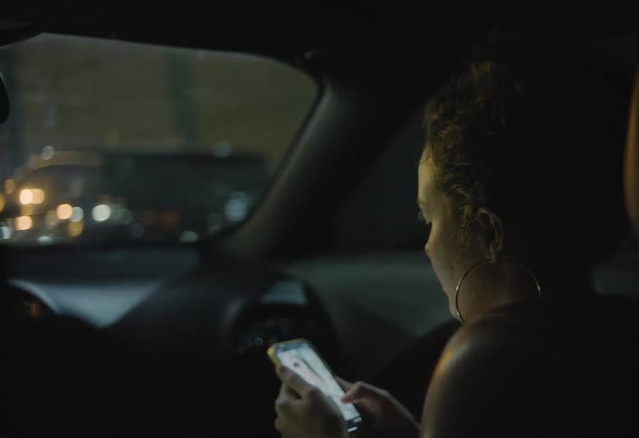Woman using her phone in the back seat of a car at night