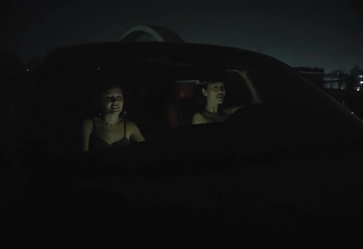 Two women smile inside a car at night during a drive