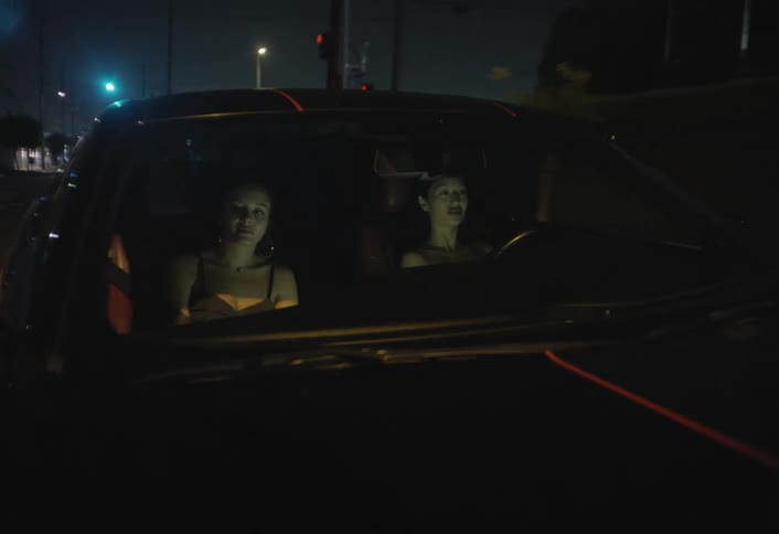 This video shows an interior view of a car at night focusing on the driver who is largely silhouettedthe driver looks from side to side and speaks with their face briefly illuminated by passing streetlights and the glow of the dashboard