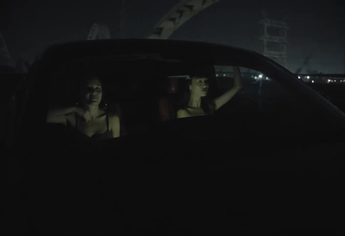 Two women drive a car over a bridge at night