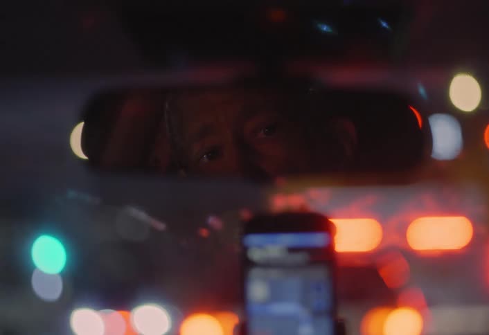Driver is reflected in the rearview mirror while driving through city lights
