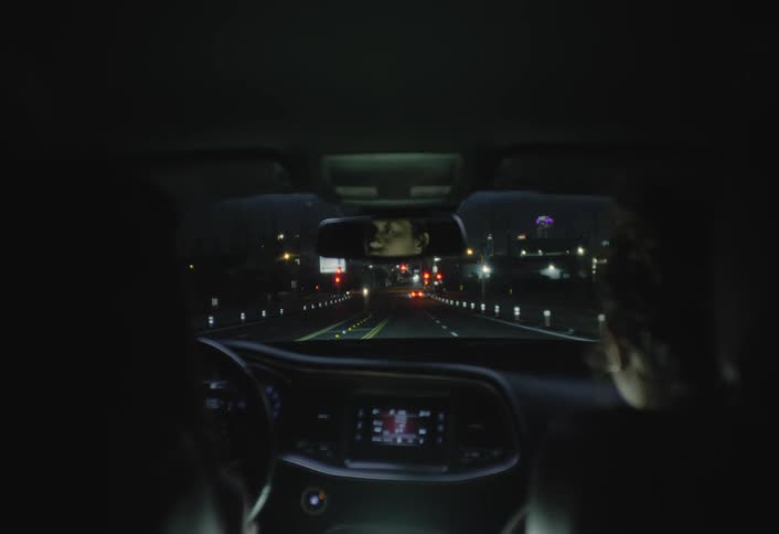 Male driver and his female passenger talk while sitting in a car as it approaches an intersection at night