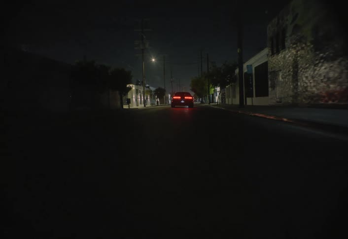 Car drives down a dark street with few lights on