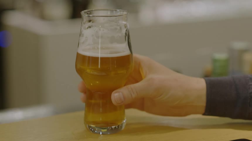 A persons hand picking up a glass full of beer from a wooden table