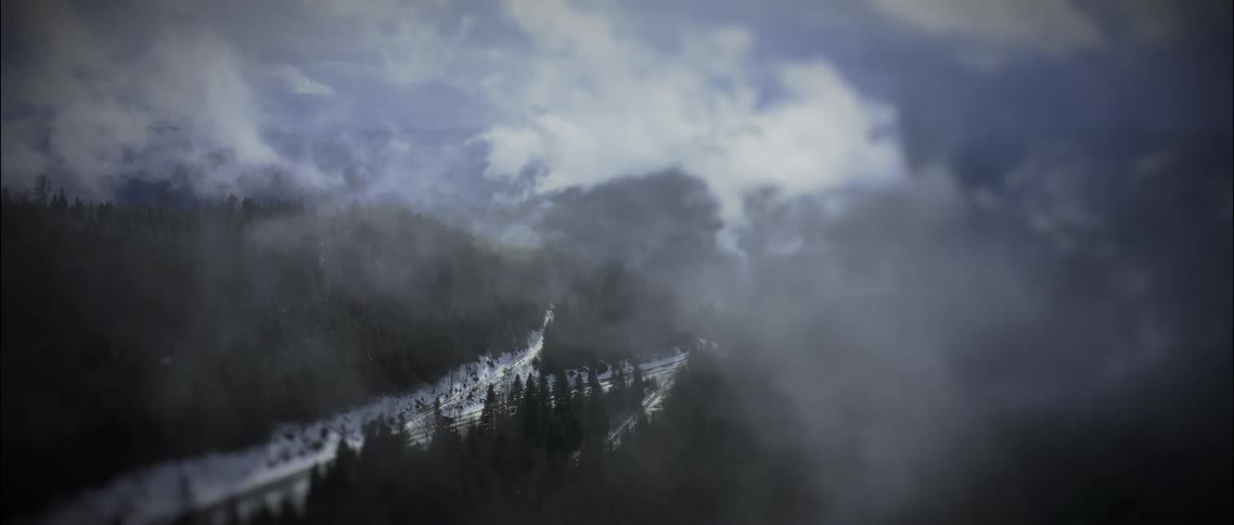 Low lying clouds cover a conifer forest and the highway passing through it