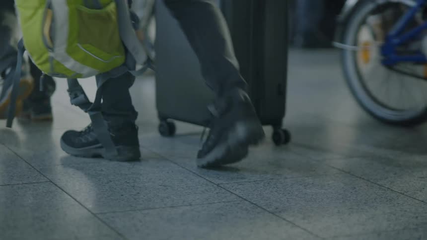 Several peoples legs are walking across a floor with checkered tiles and they are carrying backpacks