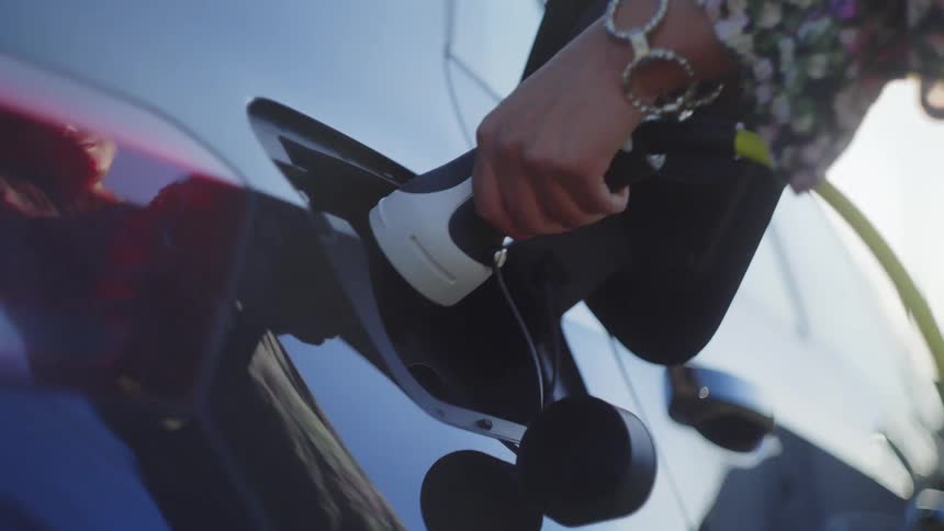 Woman removes charging cable from electric car