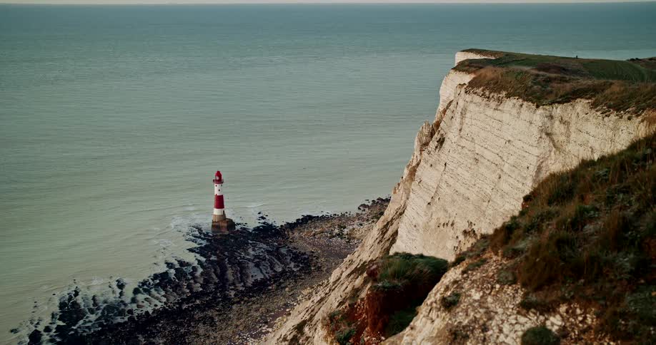 Aerial shot of red and white lighthouse stands beside a seaside cliff