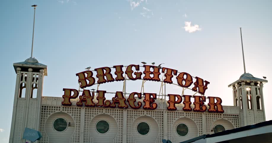 Brighton palace pier sign lit up under a blue sky with seagulls flying