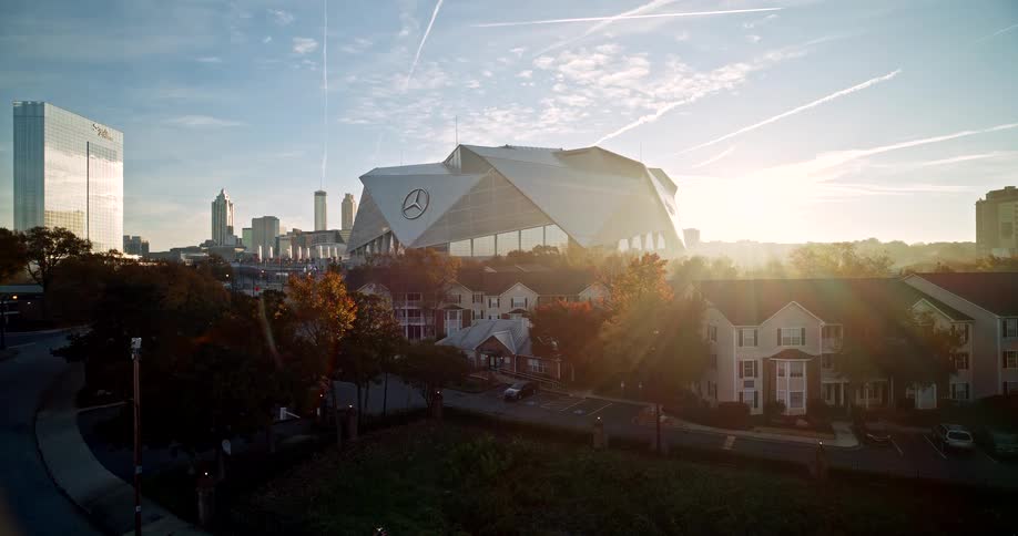 The sun rises behind mercedes benz stadium in atlanta illuminating a nearby neighborhood and the city skyline