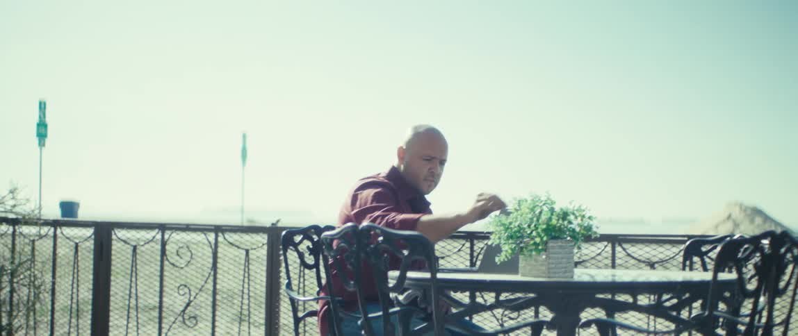 A young man using a laptop computer while sitting at a dining table outdoors during daytime