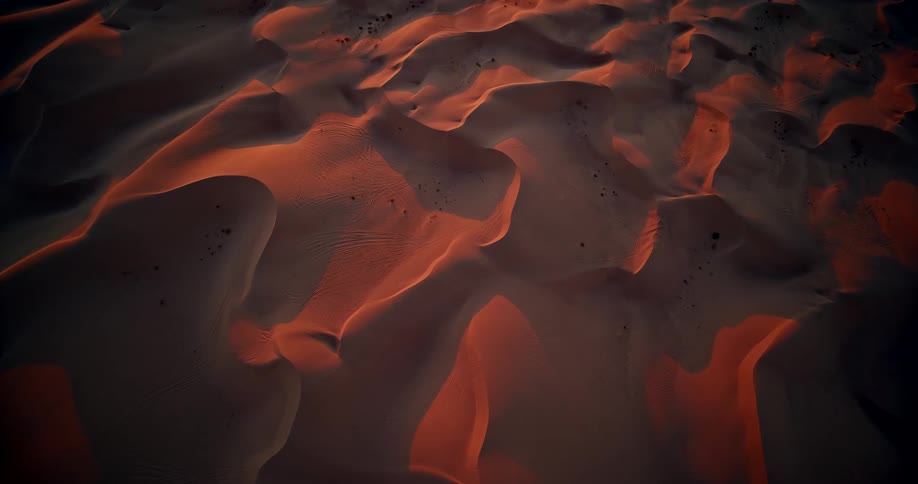 This video offers a highangle closeup view of sand dunes or sculpted sand formations most likely at dusk or sunrise the lighting creates a dramatic highcontrast effect where the deep shadows of the valleys contrast with the dune peaks catching a w
