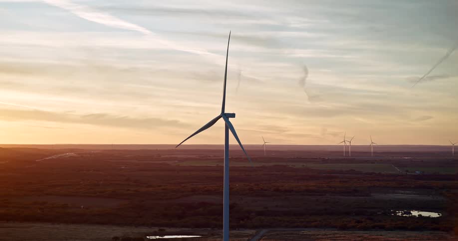 Wind turbine spins over a landscape at sunset