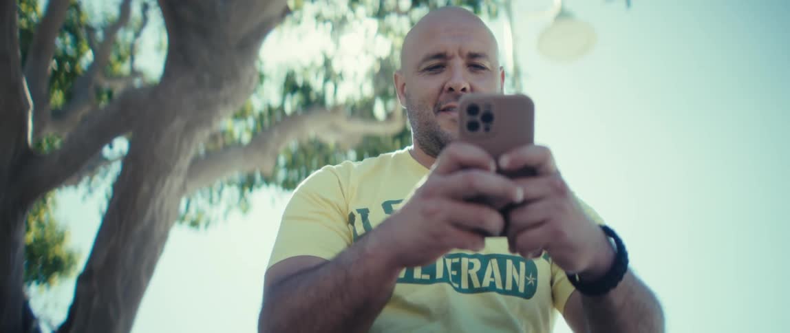A man texting with a mobile phone while sitting outdoors during daytime