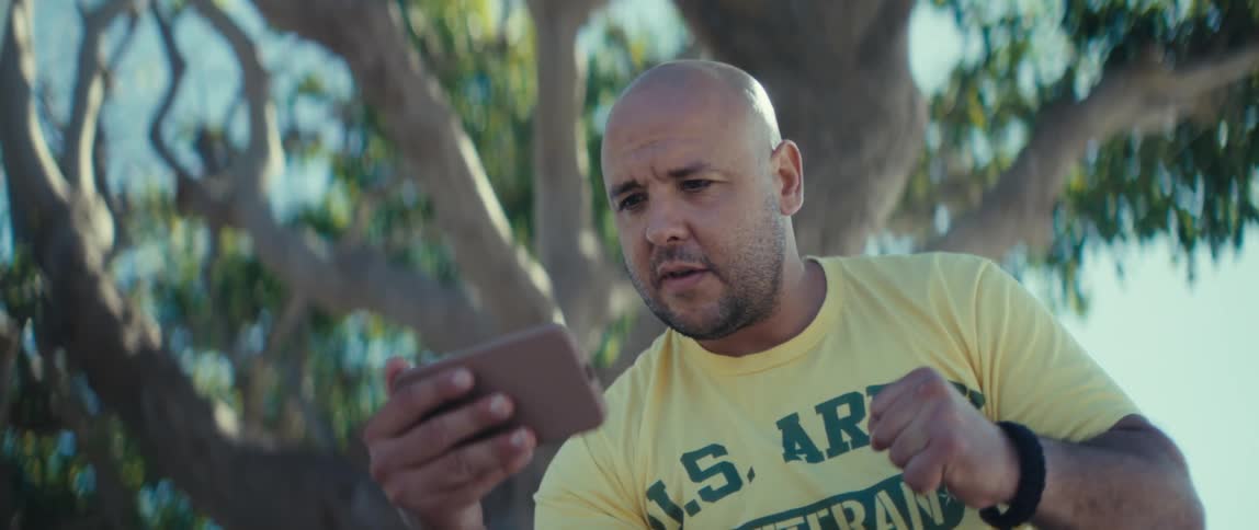 Man reacting excitedly while holding a phone in a treefilled park