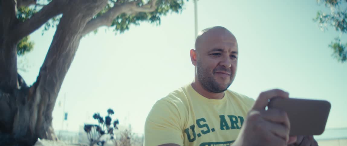 Man sitting near a tree looking at his phone on a sunny day