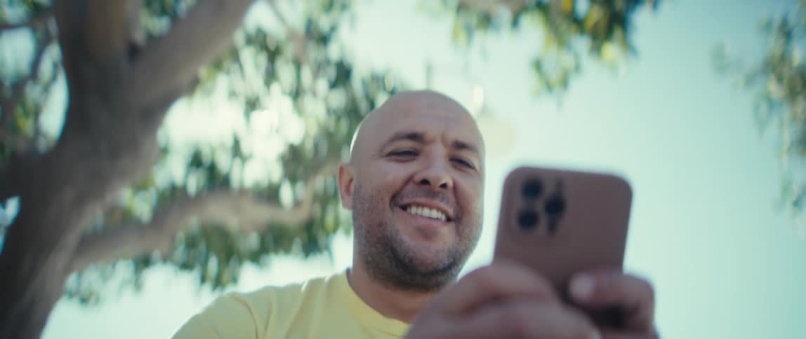 A man smiling while using a mobile phone outdoors during daytime