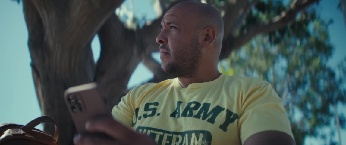 Man sitting near a tree texting on his phone