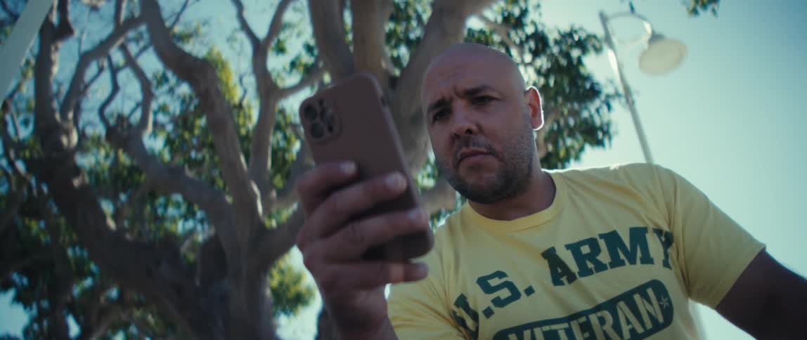 Young bald man frowning while looking at a smartphone on his hand outdoors during day time