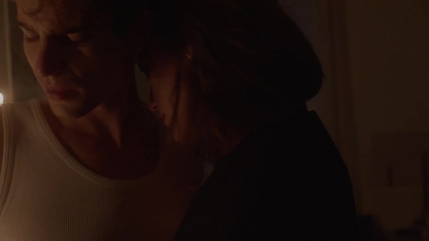 Couple in a dimly lit setting stands close together with a lit candle in the background