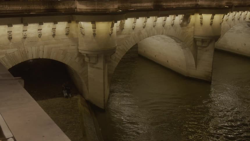 A bridge over a canal in the city is illuminated at night with a couple walking hand in hand across it