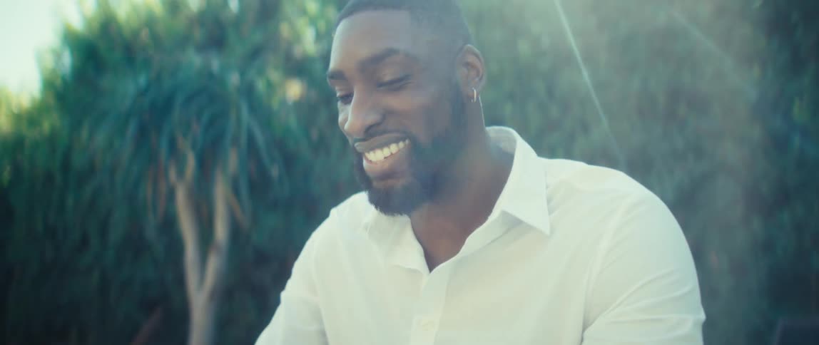 A man sitting in a backyard holding a tablet and a stylus smiles and makes a triumphant gesture with his hand signaling a breakthrough