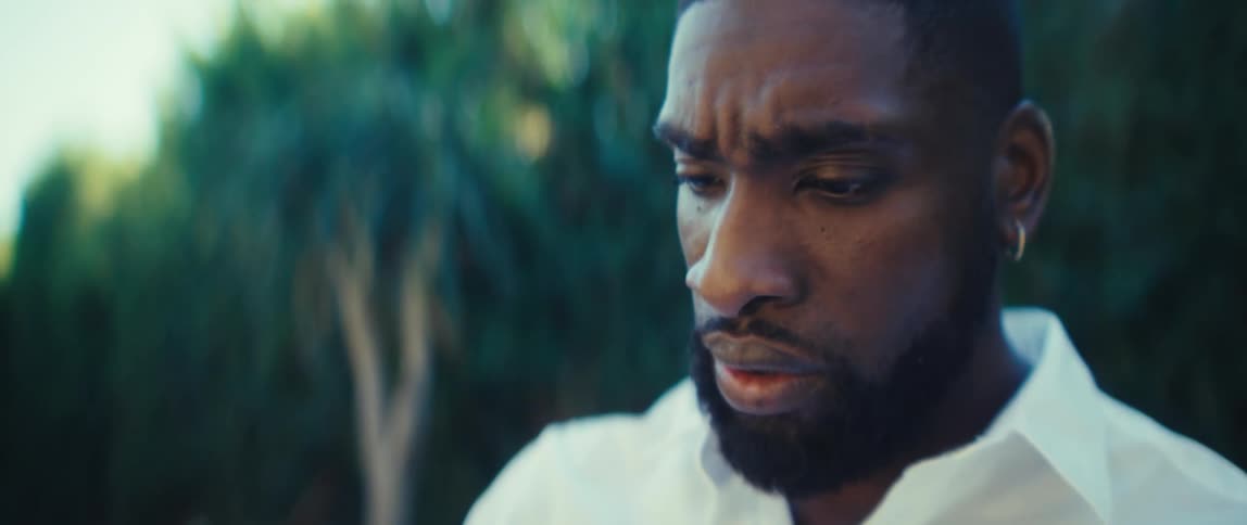 Bearded black man wearing a white shirt sitting on a chair using a tablet outdoors during day time
