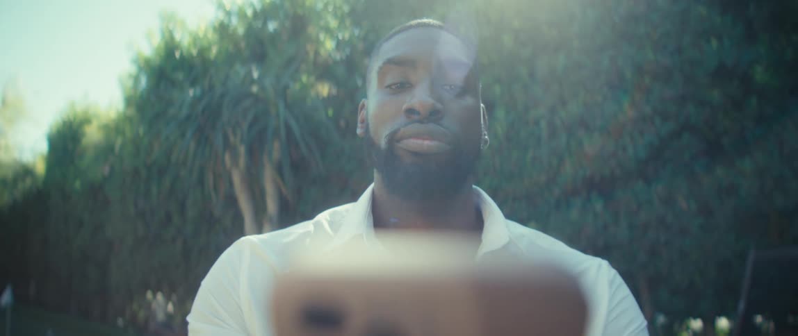 Man smiling in the sunlight while holding a phone