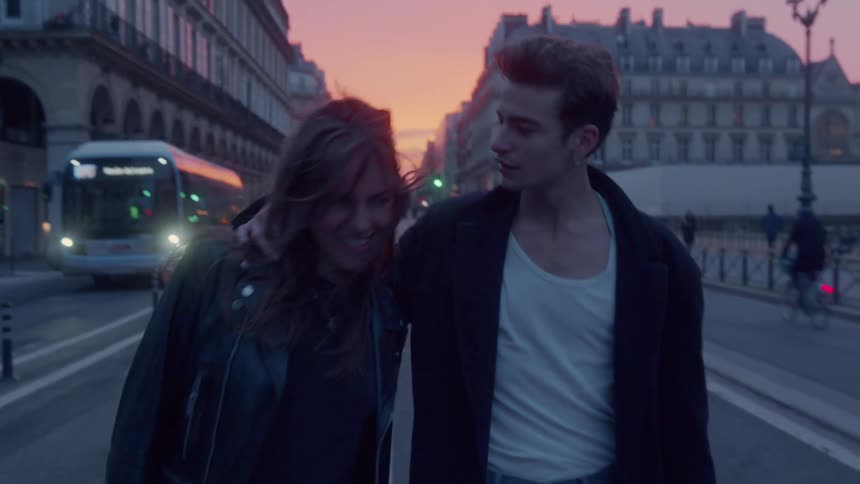 A young couple walks on a road in paris only to stop when she tries to nuzzle him then they both laugh