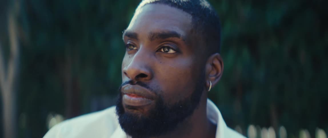 Bearded black man wearing a white shirt with a contemplative face expression outdoors during day time