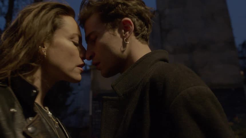 A young couple rushes toward one another in front of a monument but stop themselves trying to resist their mutual attraction yet they cant help themselves from embracing kissing and caressing each other