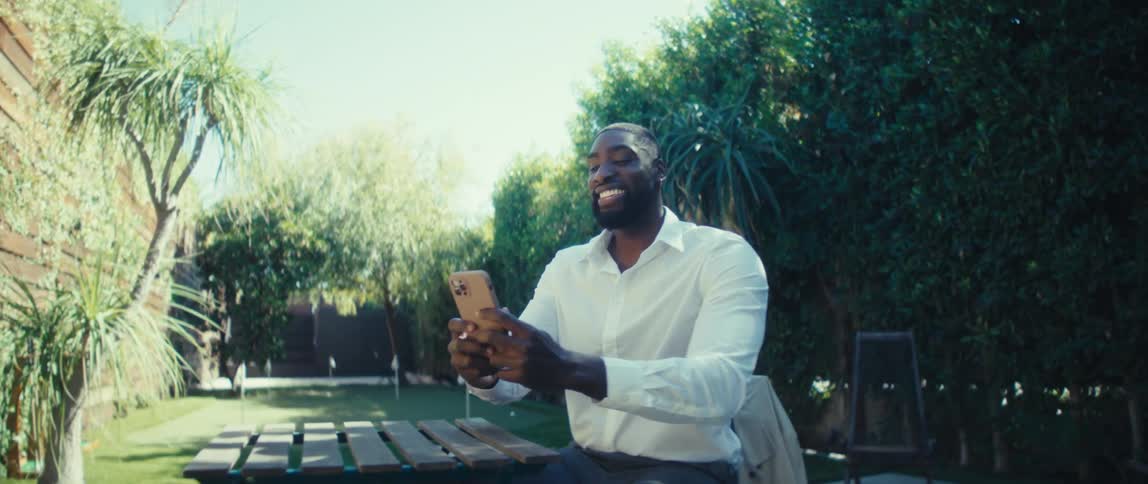 Person in a white shirt holds a smartphone in an outdoor area with a putting green in the background