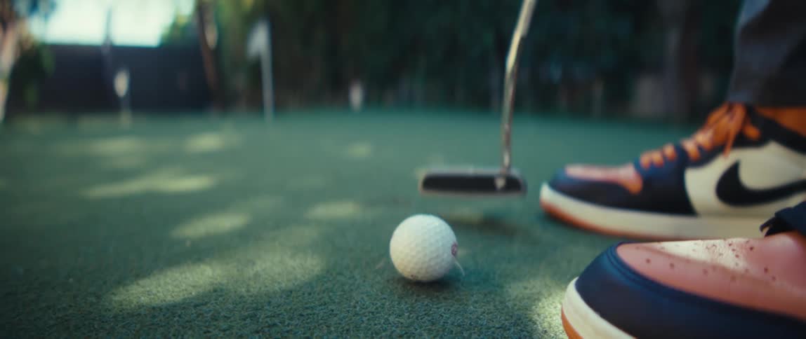 Man hits a golf ball with his golf club and it moves toward the hole