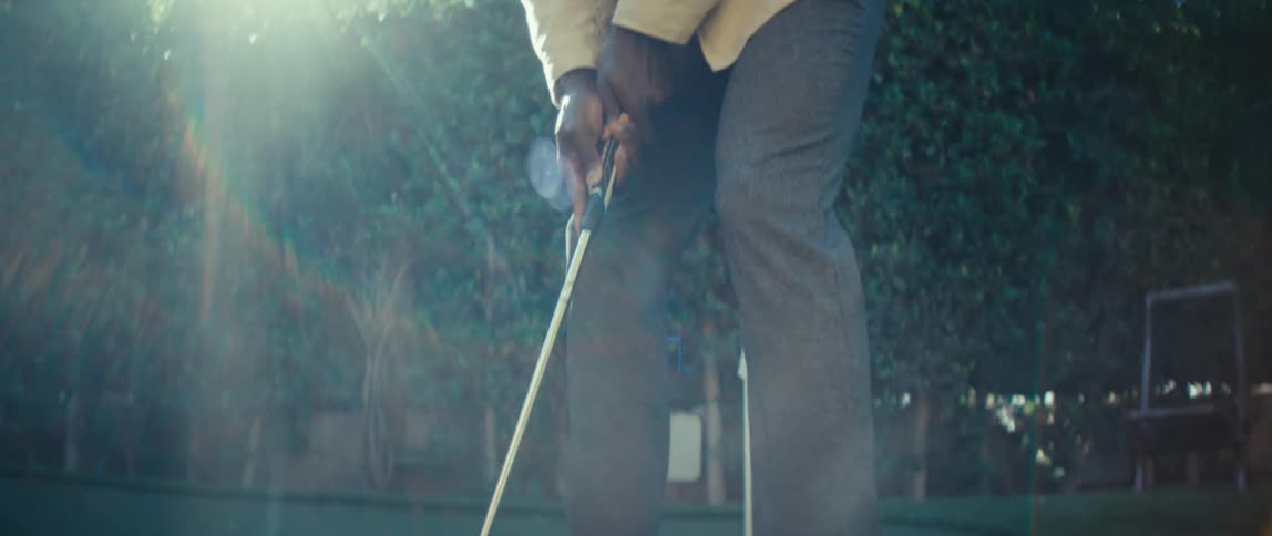 A black man putts a ball on a golf course on a sunny day