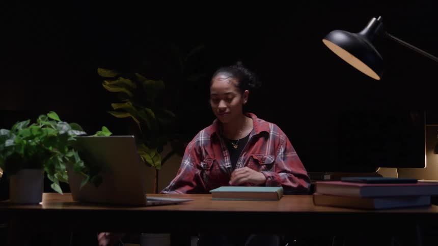 Female student puts down her backpack and then sits down to read a textbook at night