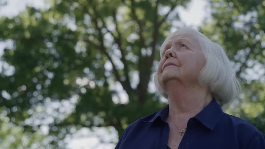 Elderly woman looks at the sky with a calm expression under the trees
