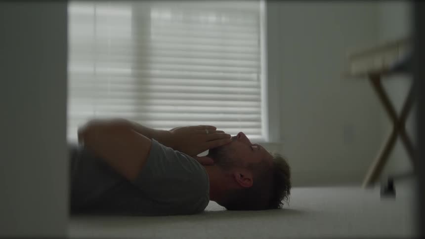 Man lying on his carpeted floor rubs his face during the daytime