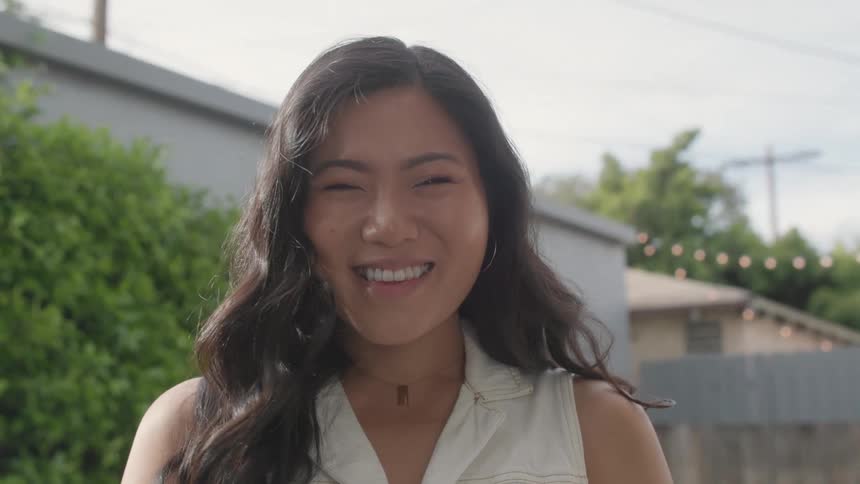 A young asian woman smiles while standing outdoors in a residential neighborhood