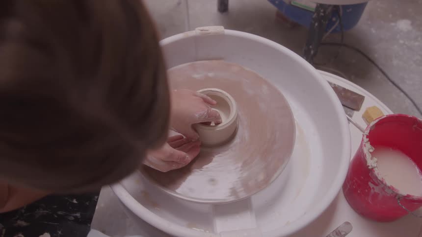 Woman shaping a small clay pot on a pottery wheel