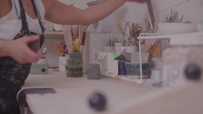 Woman picking up paintbrushes and tools on a workbench in an art studio