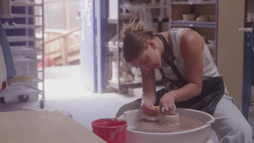 Young woman sitting in a room working with clay on a pottery wheel