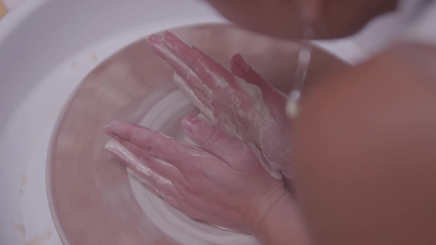 Claycovered hands shaping a piece on a spinning pottery wheel
