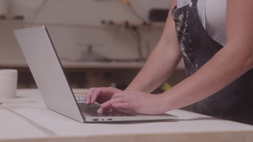 Young woman stands at a table typing on a laptop computer
